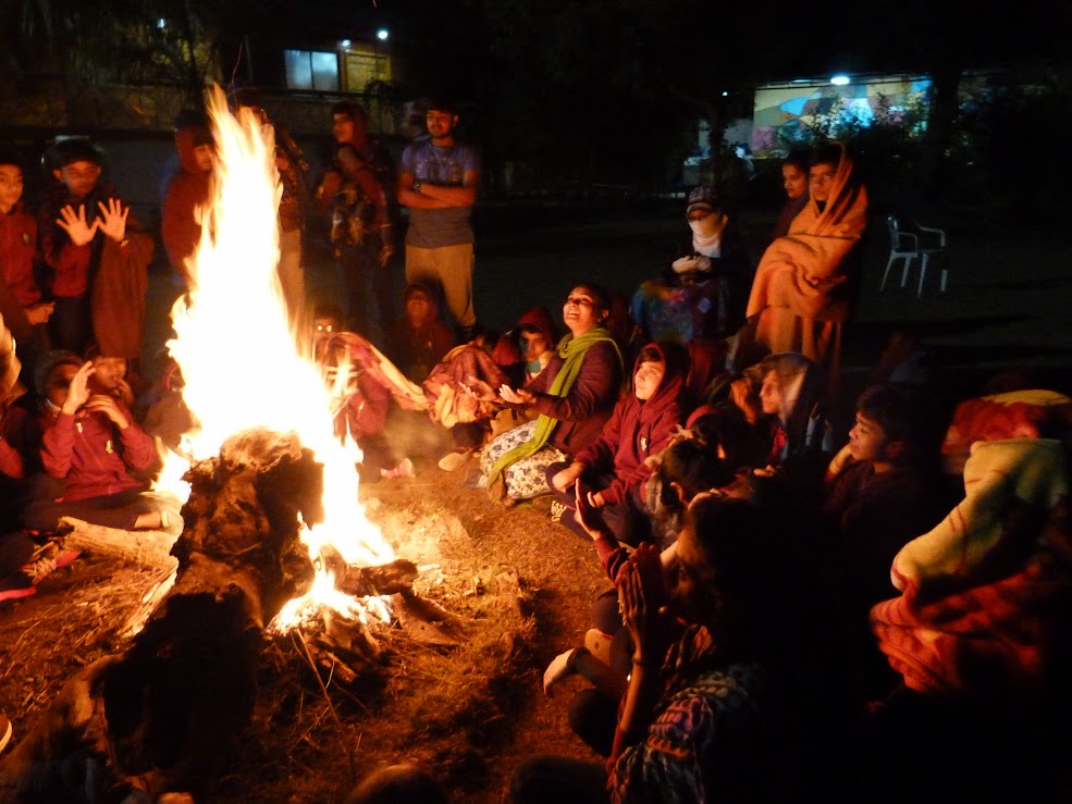 Students warming hands around a large bonfire at night