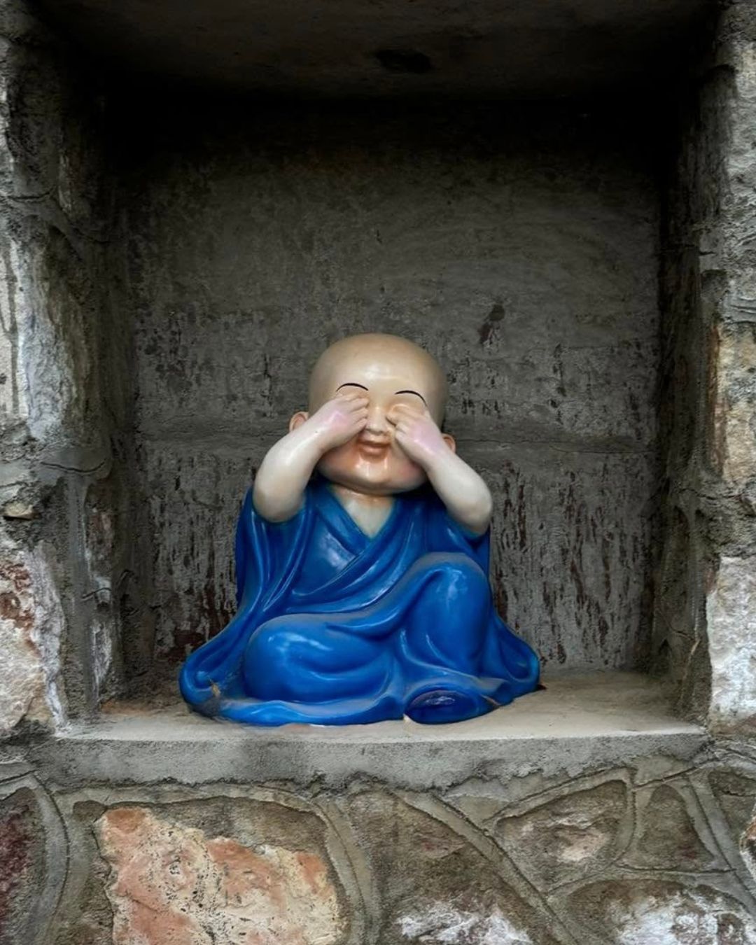 Blue robed little monk statue covering eyes see no evil pose